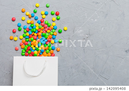 shopping paper gift bag in corner full of assorted traditional candies falling out on colored background with copy space. Happy Holidays sale concept shopping paper gift bag in corner full of assorted traditional candies falling out on colored background with copy space. Happy Holidays sale concept 142095408
