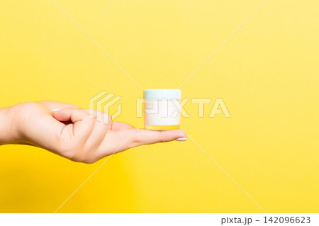 Female hand holding cream bottle of lotion isolated. Girl give jar cosmetic products on yellow background Female hand holding cream bottle of lotion isolated. Girl give jar cosmetic products on yellow background 142096623