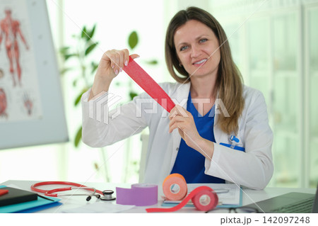 Doctor shows kinetic tape for injured joint recovery in clinic Doctor shows kinetic tape for injured joint recovery in clinic 142097248