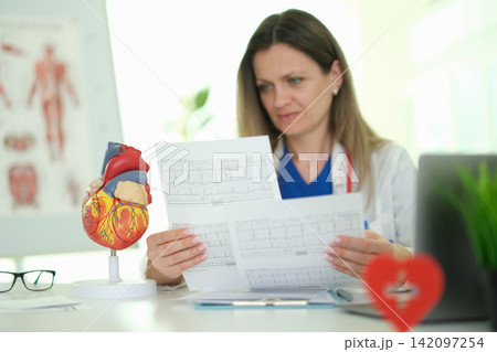 Focused female doctor reads cardiogram as sits at table in clinic 142097254