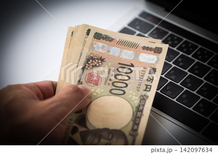 パソコンの前でお金を持つ男性の手元 パソコンの前でお金を持つ男性の手元 142097634