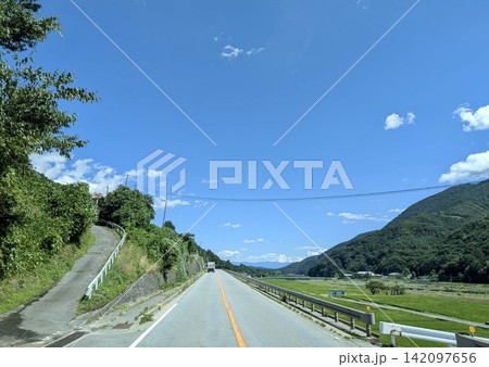 青空の下を田園と山へまっすぐ伸びる夏の道路 142097656