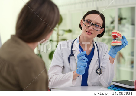 Woman doctor explains tooth model to patient during dental visit Woman doctor explains tooth model to patient during dental visit 142097931