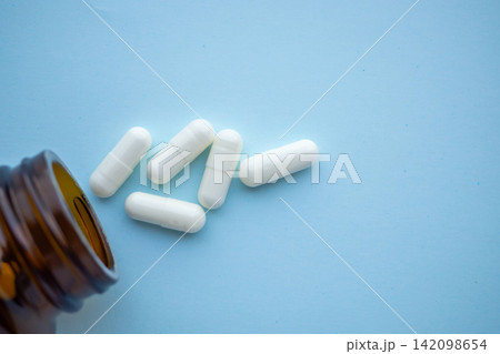 medicine pills capsule spilling out of bottle on blue background medicine pills capsule spilling out of bottle on blue background 142098654
