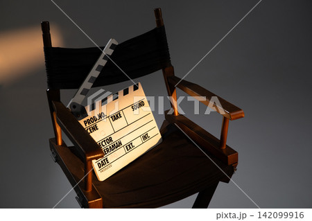 Close up of a director chair with a movie clapperboard lit by warm studio light in a dark background Close up of a director chair with a movie clapperboard lit by warm studio light in a dark background 142099916