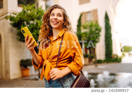Happy woman with phone in hands walks along the sea promenade, enjoying sunny day. Vacation concept. Happy woman with phone in hands walks along the sea promenade, enjoying sunny day. Vacation concept. 142099957
