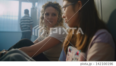 Teacher Sits Beside Withdrawn Teenage Girl on Hallway Floor 142100196