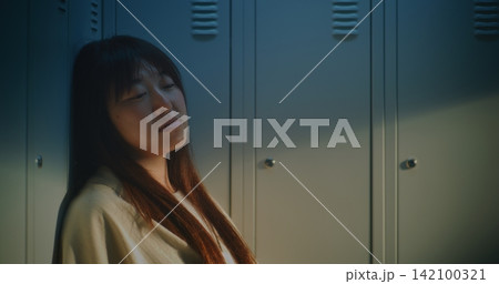 Young Woman Leaning against Lockers, Lost in Thought while Coping With Pressure, Emotional Fatigue Young Woman Leaning against Lockers, Lost in Thought while Coping With Pressure, Emotional Fatigue 142100321