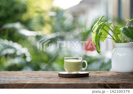 Matcha in a glass cup and philodendron plant pot on brown wooden table Matcha in a glass cup and philodendron plant pot on brown wooden table 142100379