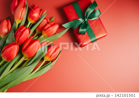 Mothers' day. Red tulips with gift box. Easter holiday. Red background, copy space. 142101501