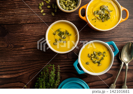 Pumpkin soup in ceramic bowls, wooden background, fresh pumpkins. Autumn food, copy space Pumpkin soup in ceramic bowls, wooden background, fresh pumpkins. Autumn food, copy space 142101681