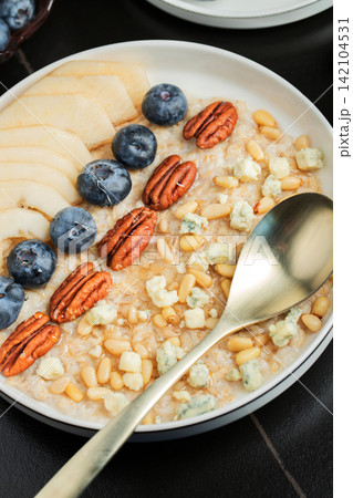 Oatmeal. Bowl of oatmeal porridge with blackberry, bananas and chia seeds on gray concrete old table background. Top view in flat lay style. Natural ingredients. Hot healthy breakfast and diet food Oatmeal. Bowl of oatmeal porridge with blackberry, bananas and chia seeds on gray concrete old table background. Top view in flat lay style. Natural ingredients. Hot healthy breakfast and diet food 142104531