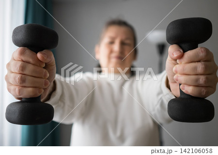 Woman holding dumbbells toward the camera in a home workout scene Woman holding dumbbells toward the camera in a home workout scene 142106058