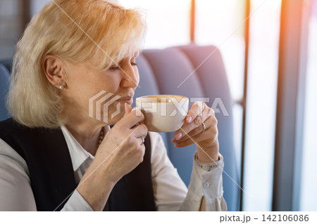 Elderly Woman Relishes Fragrant Brew. Aging Woman Savoring Fragrant Aroma Of Steaming Coffee In Sunlight. An Older Woman Peacefully Delights In Rich Aroma Of Freshly Brewed Coffee Outdoors 142106086