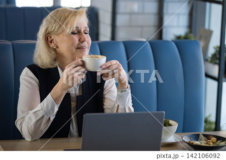 Businesswoman Reviewing Schedule. Focused Businesswoman Analyzing Plans On Laptop. Woman In Business Attire Examining Her Schedule On Laptop In Cheerful Cafe Environment With Documents 142106092