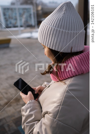 Pregnant woman in winter hat and scarf holding a smartphone while sitting indoors Pregnant woman in winter hat and scarf holding a smartphone while sitting indoors 142106101