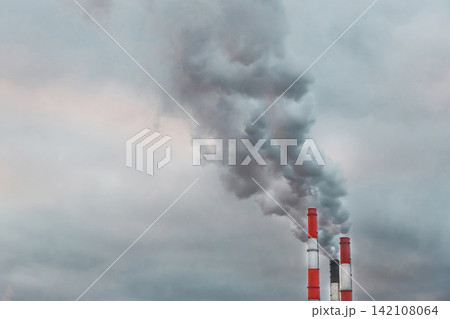 Problems of environmental pollution and ecology. Dark gray acrid smoke comes from a chimney of an industrial plant or thermal power plant against the background of the sky Problems of environmental pollution and ecology. Dark gray acrid smoke comes from a chimney of an industrial plant or thermal power plant against the background of the sky 142108064