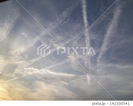 夕暮れの空に交差する飛行機雲と幻想的な雲 夕暮れの空に交差する飛行機雲と幻想的な雲 142108541