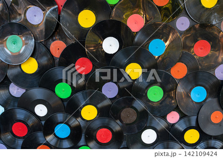 Abstract music background shows variety of old black vinyl records with bright colorful round stickers overlapping to create decorative wall texture. Abstract music background shows variety of old black vinyl records with bright colorful round stickers overlapping to create decorative wall texture. 142109424