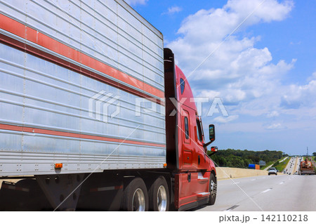 Large red truck drives along busy highway with other vehicles visible. Large red truck drives along busy highway with other vehicles visible. 142110218