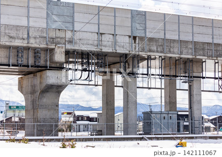 大寒波の日の加賀温泉駅付近の街並みと北陸新幹線の高架橋、雪山の冬景色 142111067