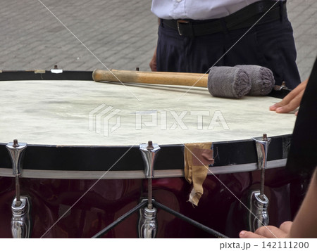 Large ceremonial bass drum with mallets rests on top as band member prepares to perform during parade festivities 142111200