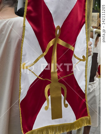 Close up of a red and white satin flag with gold trim and dagger symbol held by a participant in a historical tunic during a festival 142111205