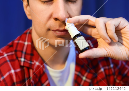 sick man using a nasal spray for cold and flu treatment. Applying medicine to his nose for allergy or respiratory illness relief. sick man using a nasal spray for cold and flu treatment. Applying medicine to his nose for allergy or respiratory illness relief. 142112442