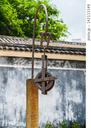 Vintage rusted iron pulley system of an ancient water well built in 1869 inside traditional Mandarin House courtyard 142113149