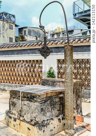 Ancient stone water well with iron pulley in Mandarin House with modern buildings background Ancient stone water well with iron pulley in Mandarin House with modern buildings background 142113150