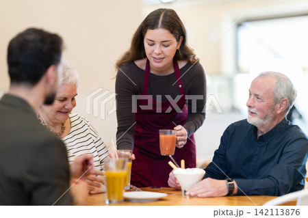 In restaurant hall, girl waiter brought order drink juice to senior family In restaurant hall, girl waiter brought order drink juice to senior family 142113876