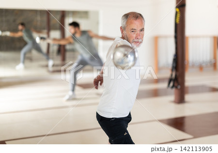 Elderly man practicing fencing movements in gym Elderly man practicing fencing movements in gym 142113905