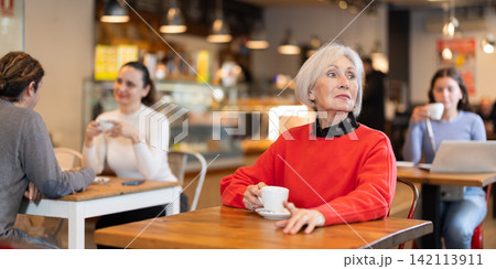 Senior woman whiles away time and waits for meeting in chain cafe 142113911