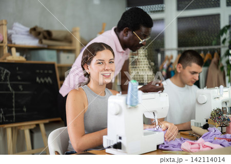 Engaged girl stitching fabric on machine in sewing class for adults 142114014