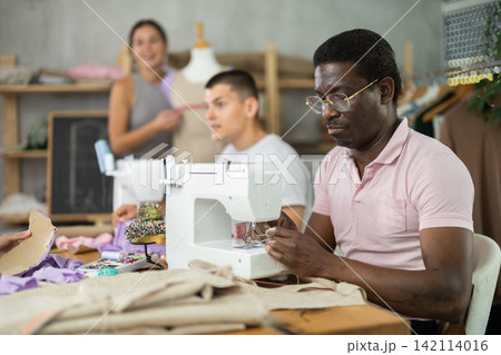 Middle-aged man stitching at machine during sewing class for adults Middle-aged man stitching at machine during sewing class for adults 142114016