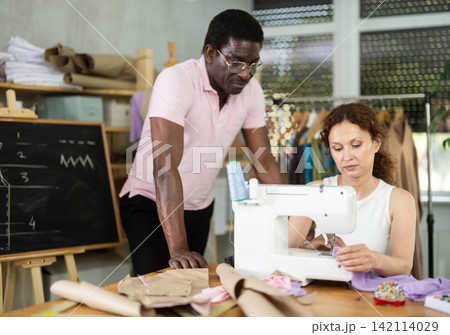 Middle-aged male teacher helping students sew Middle-aged male teacher helping students sew 142114029
