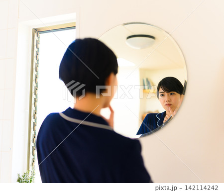鏡を見て身だしなみを整える若い女性 鏡を見て身だしなみを整える若い女性 142114242
