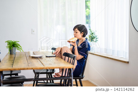 朝食中にスマートフォンを確認する若い女性 朝食中にスマートフォンを確認する若い女性 142114262