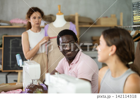 Middle-aged man talking with woman and sewing, other working with mannequin 142114318