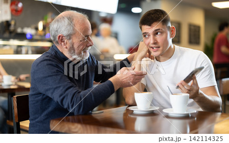 Elderly man comforts an upset guy while sitting at table in cafe 142114325