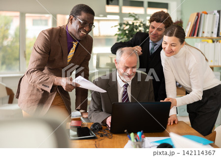 Group of colleagues look at laptop screen and laugh 142114367