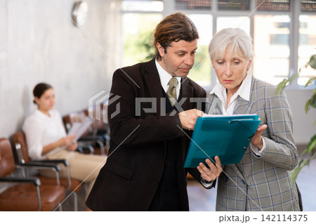 Man discussing working documents with senior female colleague 142114375