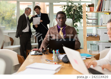 Confident man working online while checking reports of subordinates during a meeting in company office Confident man working online while checking reports of subordinates during a meeting in company office 142114420
