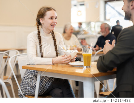 Mature father chats with his teenage daughter at a cafe table for breakfast with ice cream Mature father chats with his teenage daughter at a cafe table for breakfast with ice cream 142114458