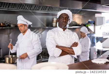 Self-confident chef manages team of chefs in restaurant kitchen Self-confident chef manages team of chefs in restaurant kitchen 142114533