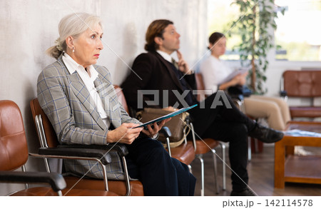 Focused aged businesswoman waiting for meeting with investors in office Focused aged businesswoman waiting for meeting with investors in office 142114578