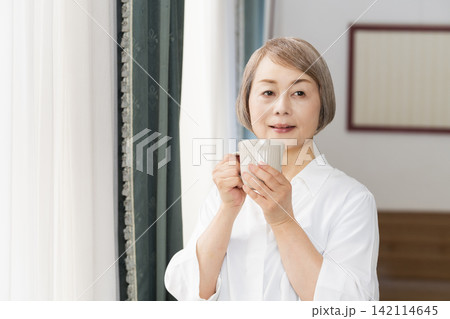 リビングの窓辺でコーヒーを飲むシニア女性 142114645