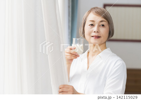 リビングの窓辺で牛乳を飲むシニア女性 142115029