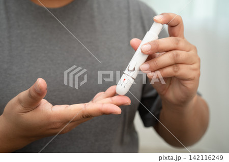Asian woman self testing to check blood sugar level diabetes by digital lancet on finger at home. 142116249