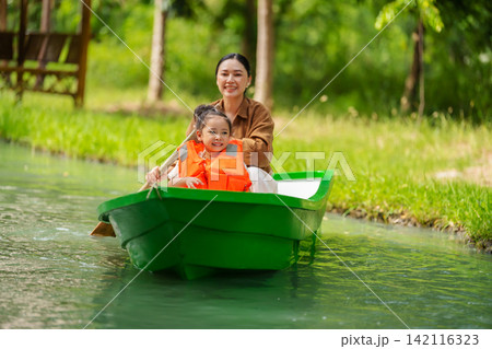 mother and preschool child girl in a green paddle boat on a scenic pond. 142116323